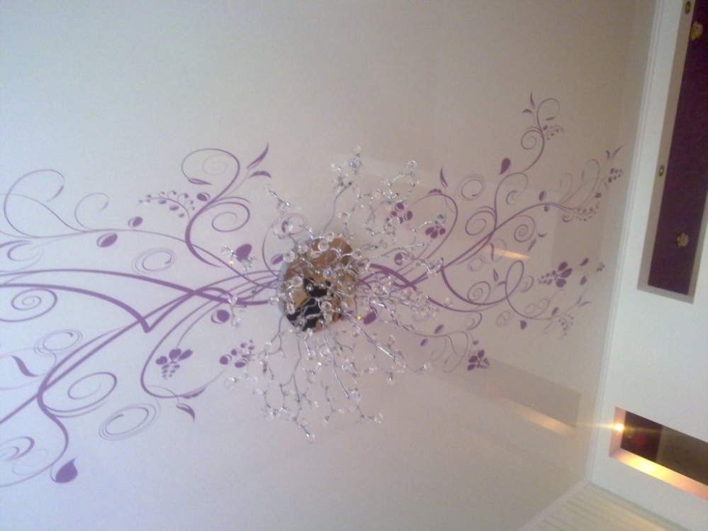 Натяжной потолок с ярким орнаментом фиолетового цвета перекликается с люстрой и создает необычный эффект 