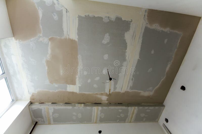 Room under repair or building of new house or apartement. Suspended rough white ceiling of drywall not finished with spots. Of plaster and electrical cords for stock image